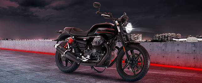 Schwarze Moto Guzzi V7 auf in einem Parkhaus vor einer Stadtkulisse.